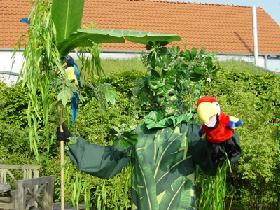 Zu dem Kostüm gehört auch ein Stab mit großen Bananen- und Bambusblättern. Desweiteren ein Papagei und eine Schlange, sowie zwei Vögel die mit den Flügel schlagen.